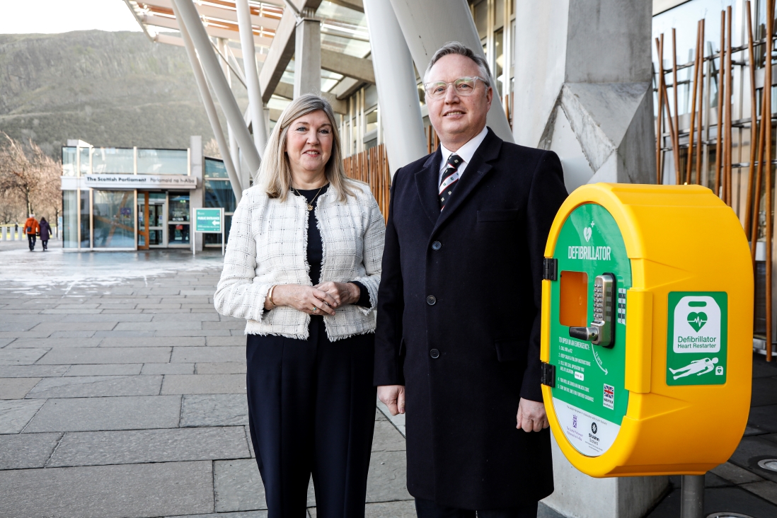 Presiding Officer Alison Johnstone and Barri Millar standing next to the new defibrillator outside the Scottish Parliament building.