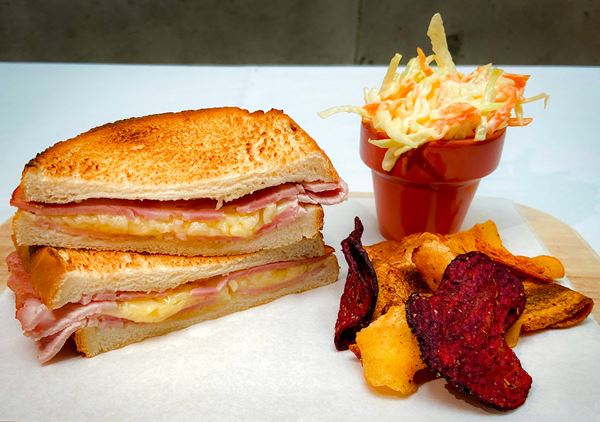 a toasted cheese and ham sandwich, with a side of coleslaw and veggie crisps